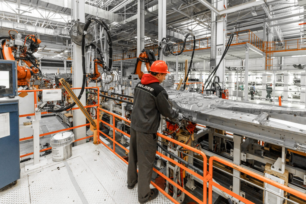 Photo of automobile production line. Welding car body. Modern car assembly plant. Auto industry. Male worker in an orange protective helmet.